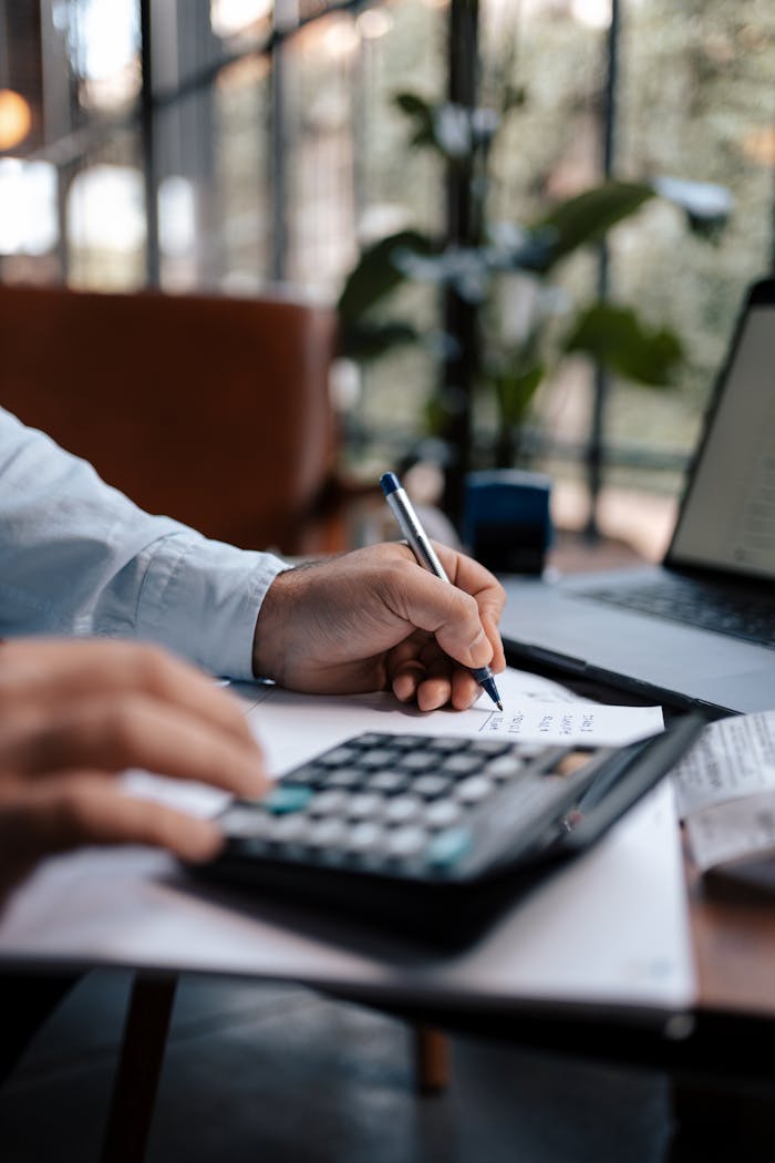 Offerings A person calculating finances with a calculator and pen on a desk indoors.