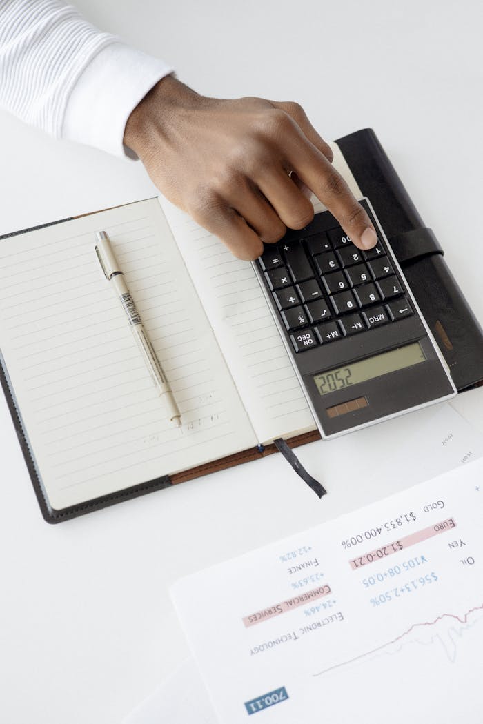 Home A hand using a calculator with financial documents and notebook, depicting an office setup for financial analysis.