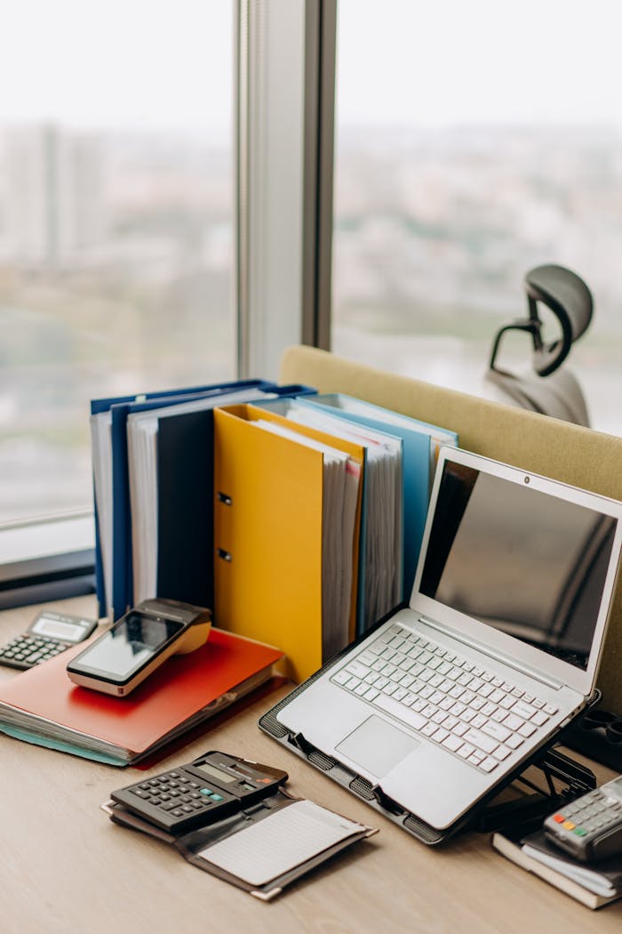 Services Modern workplace setup with laptop, folders, and gadgets by a window view.