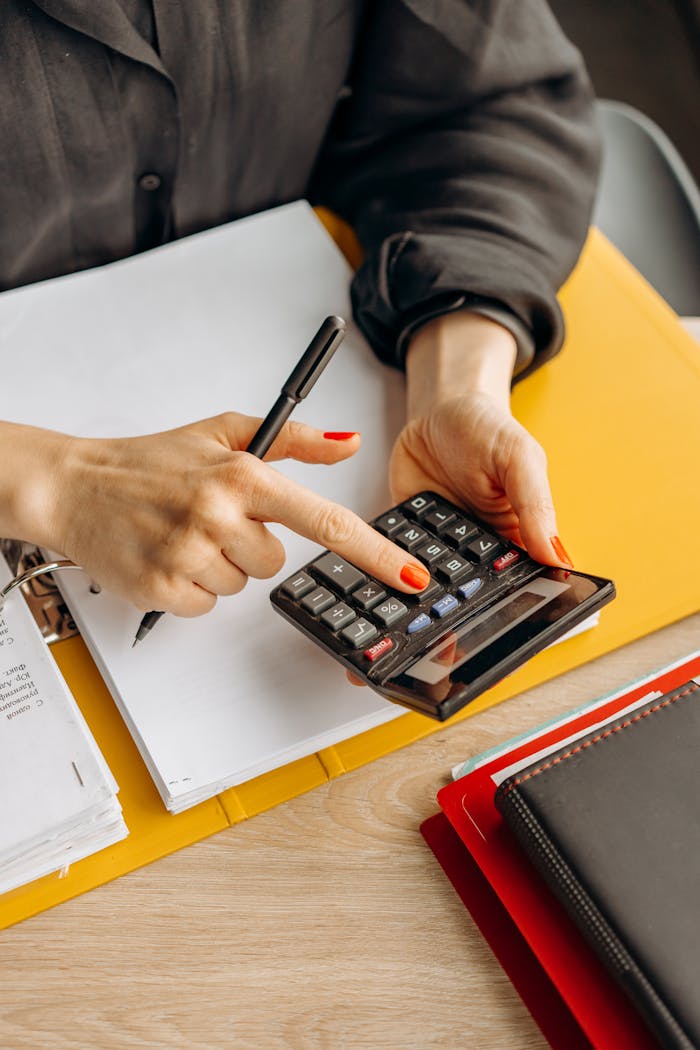 Home Close-up of a woman using a calculator at her wooden workspace with documents and notepads.